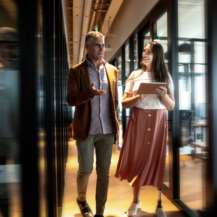 A woman and man walking in a hallway and using a tablet